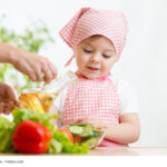Kleines Mädchen hilft der Mutter beim Zubereiten von Salat