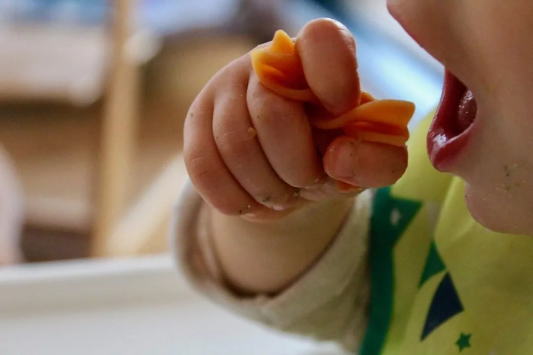 Baby hält eine Nudel in der Hand