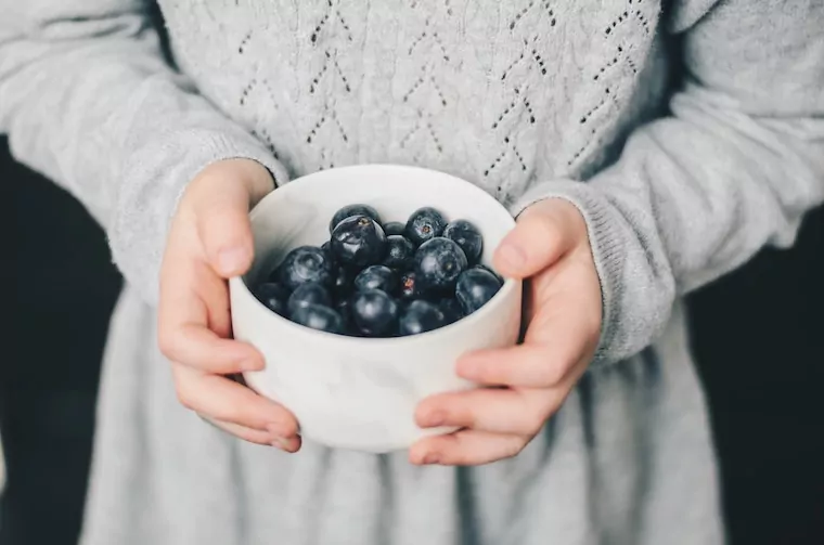 Frau hält eine Schale mit Heidelbeeren in der Hand