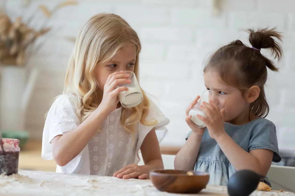 Zwei Mädchen trinken Milch aus Gläsern.