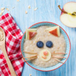 Porridge in einer Schüssel, kreativ drapiert mit Obst in Form eines Katzengesichts