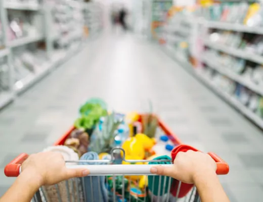 Frauenhände schieben einen Einkaufswagen durch einen Supermarkt