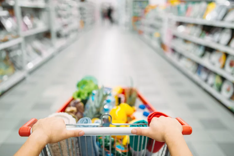 Frauenhände schieben einen Einkaufswagen durch einen Supermarkt