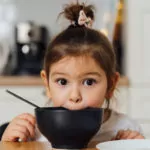 Kleines Mädchen vor einer Schüssel am Tisch
