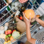Kinderhände, die eine Grapefruit in einen gefüllten Einkaufwagen legen
