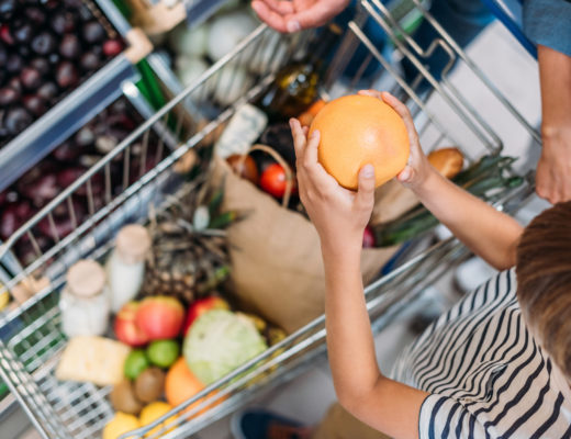 Kinderhände, die eine Grapefruit in einen gefüllten Einkaufwagen legen