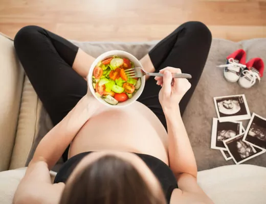 Schwangere Frau isst eine Salat-Bowl auf dem Sofa