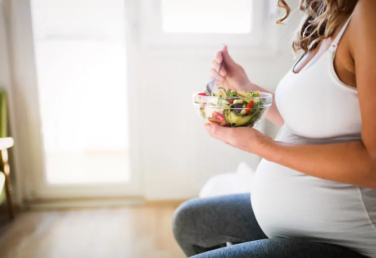 Schwangere Frau isst eine Schüssel Salat.