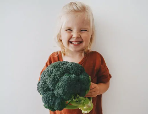 Mädchen hält einen Brokkoli in der Hand und lacht in die Kamera