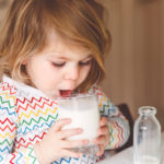 Kleines Mädchen trinkt ein Glas Milch.