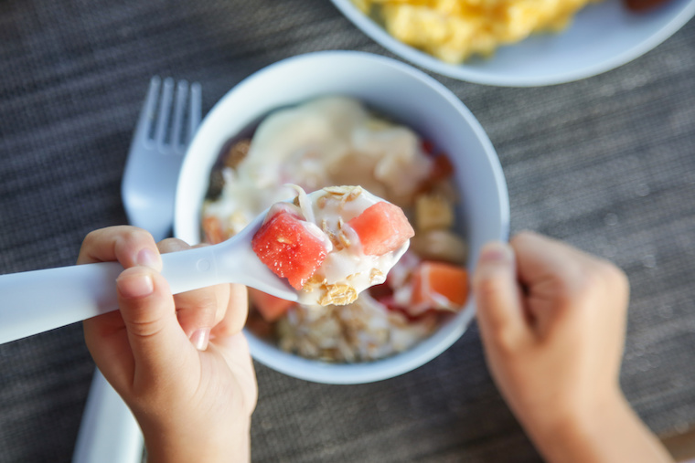 Kind isst ein Müsli mit Früchten und Joghurt