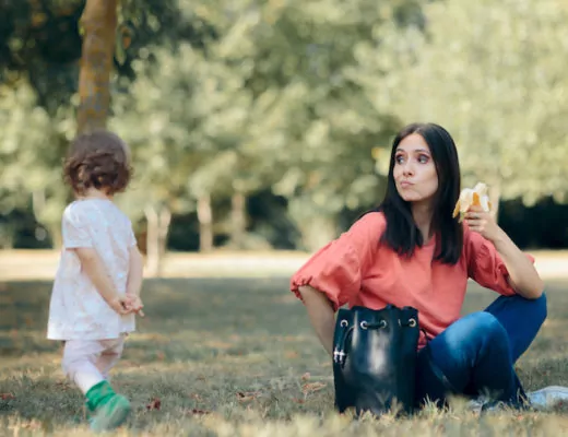 Mutter mit Banane in der Hand sieht Kleinkind zu wie es wegläuft