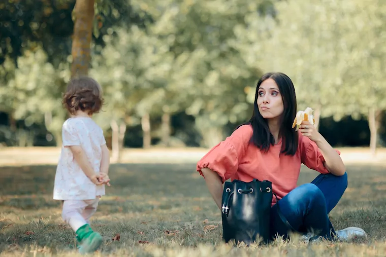 Mutter mit Banane in der Hand sieht Kleinkind zu wie es wegläuft