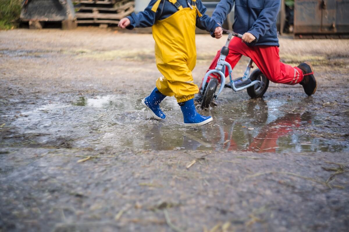 Kinderfüße in Gummistiefel, die in eine Pfütze springen