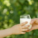 Eine Kinderhand und eine Erwachsenenhand greifen beide nach einem Glas mit Milch.