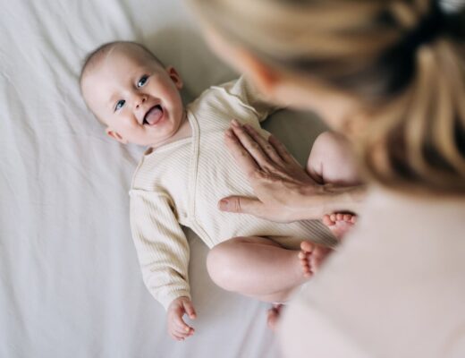 Mutter beugt sich über ein Baby in beigen Body, Vitamin D Gabe ist wichtig für Babys.