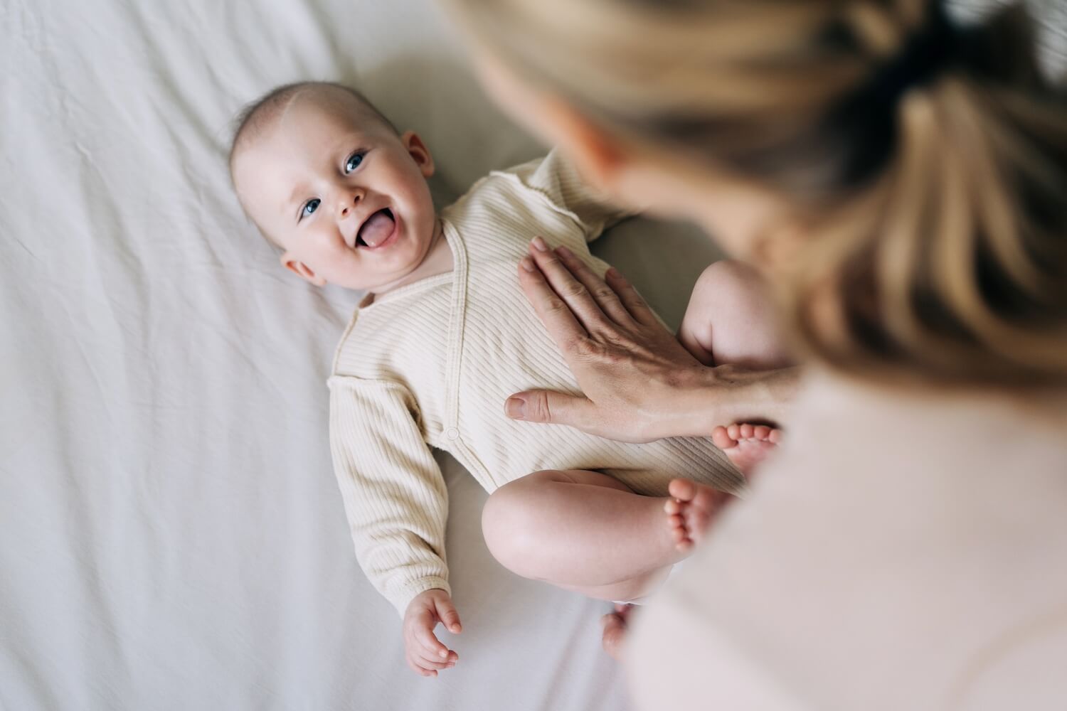 Mutter beugt sich über ein Baby in beigen Body, Vitamin D Gabe ist wichtig für Babys.