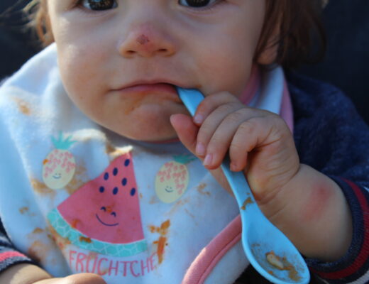 Baby mit Löffel im Mund und mit Brei verschmiertem Mund im Close-up