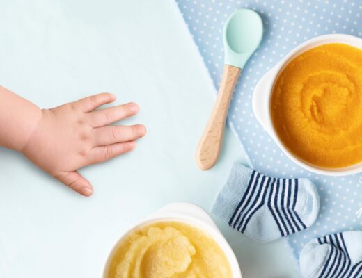 Babyhand greift nach einer Schüssel mit orangefarbenem Möhren-Brei