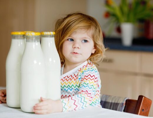 Kleinkind sitzt am Tisch und hält 3 Flaschen mit Milch im Arm