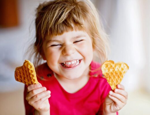 Ein Mädchen hält zwei Herzwaffeln in der Hand und lacht.